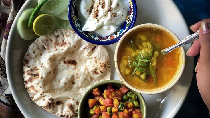 Platter of flatbread, soup, and side dishes on a blue surface with a patterned cloth.