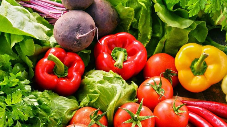 Assorted fresh vegetables including carrots, tomatoes, bell peppers, and lettuce on a wooden surface.