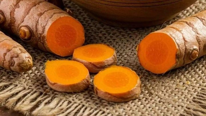 Turmeric powder in a wooden bowl with turmeric roots and a pestle on a brown background
